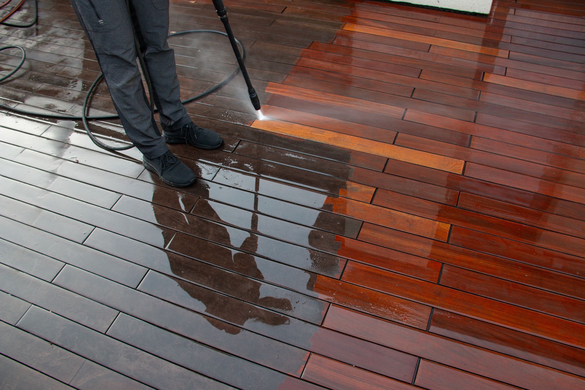 A person is cleaning a wooden deck with a high pressure washer.
