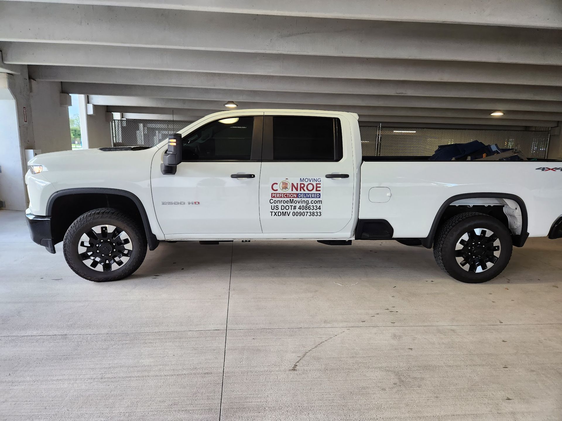 A white truck is parked under a bridge in a parking garage.