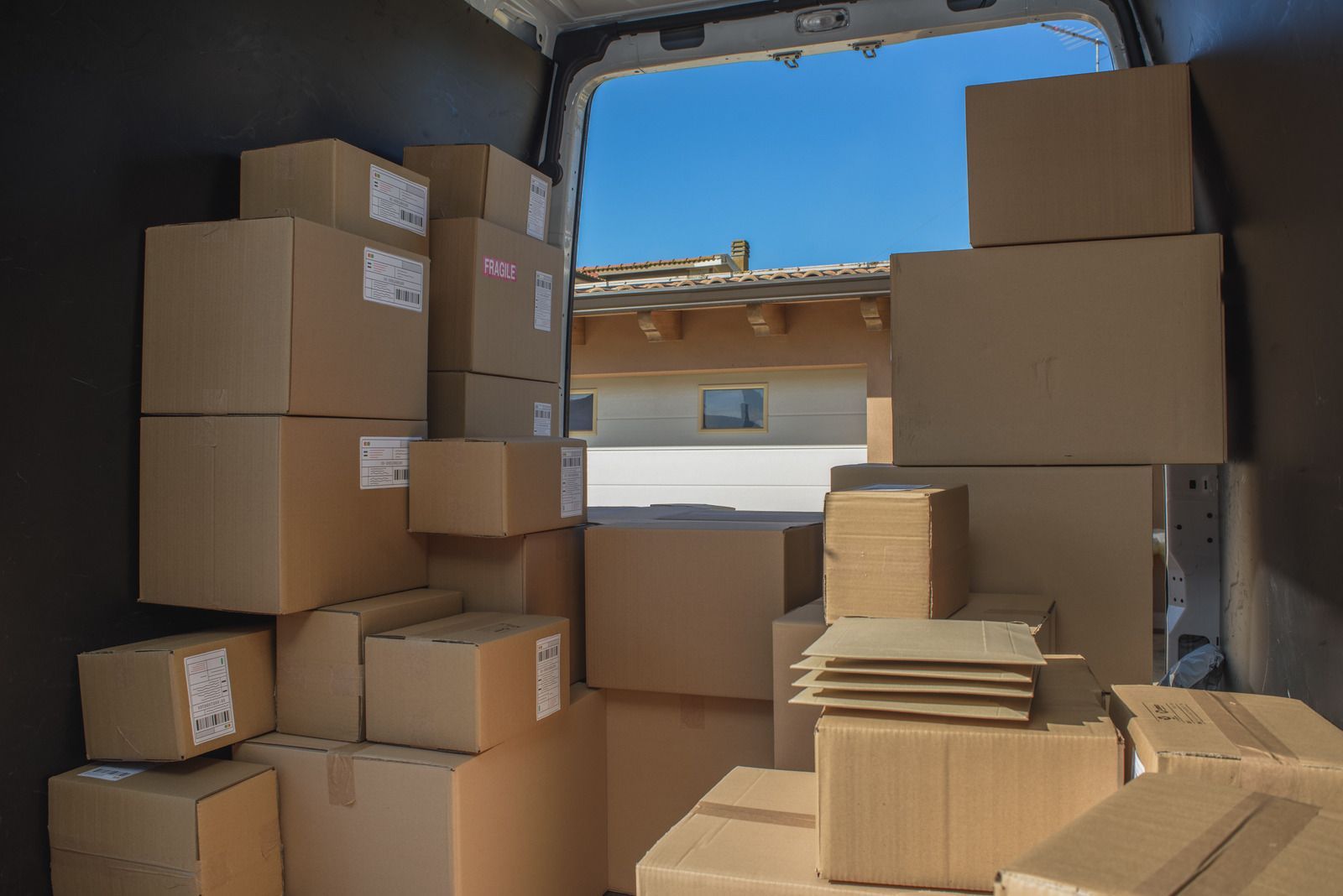 The back of a delivery van is filled with lots of cardboard boxes.