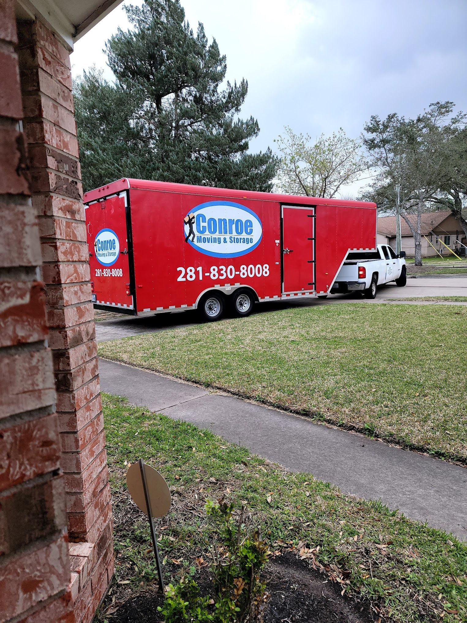 A red trailer is parked in front of a brick house.