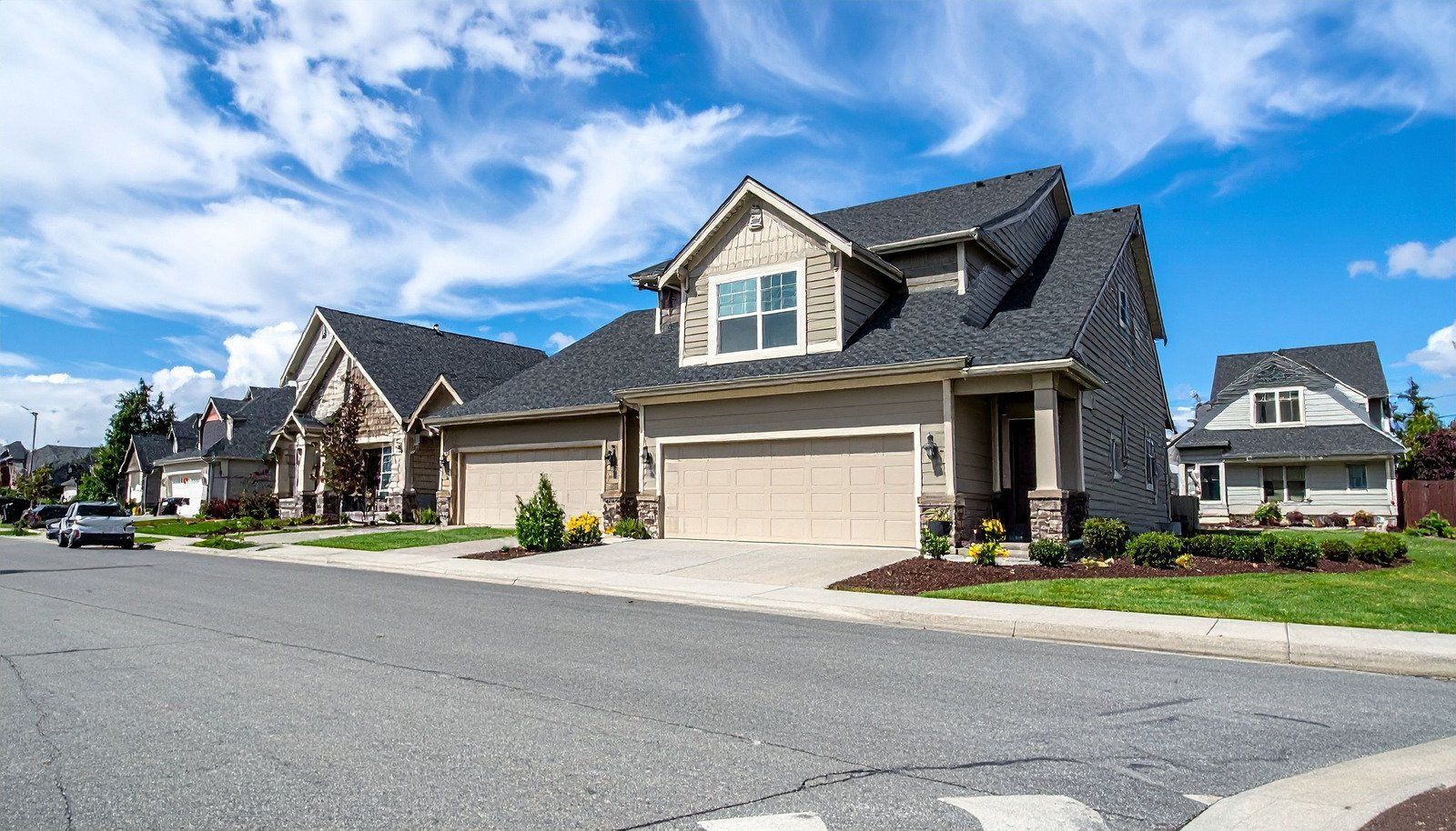 Row of suburban homes with gray asphalt road and blue sky.