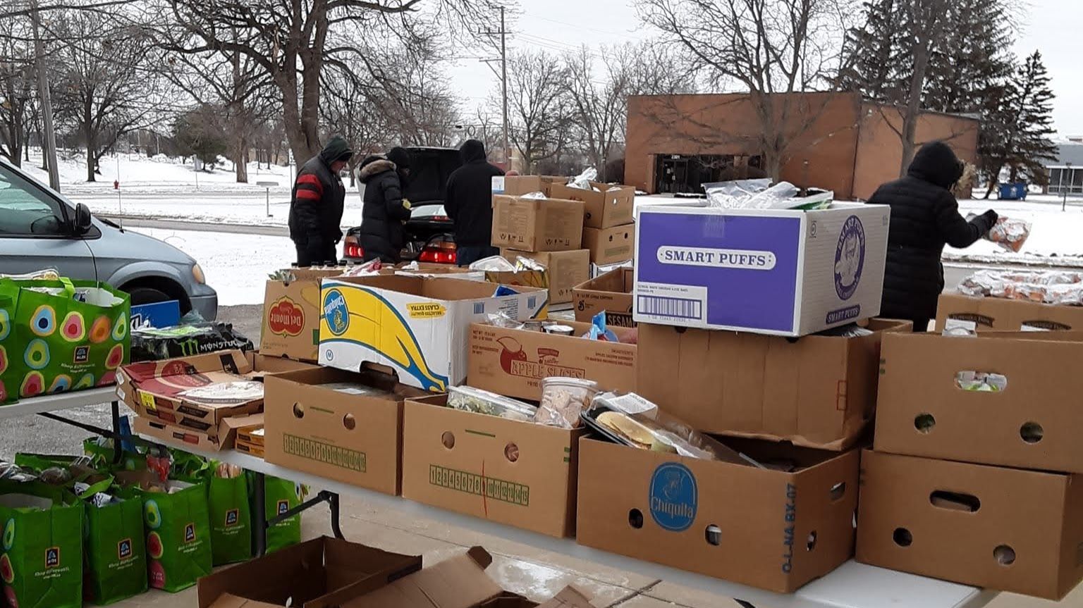 A group of people are standing around a table filled with boxes of food.