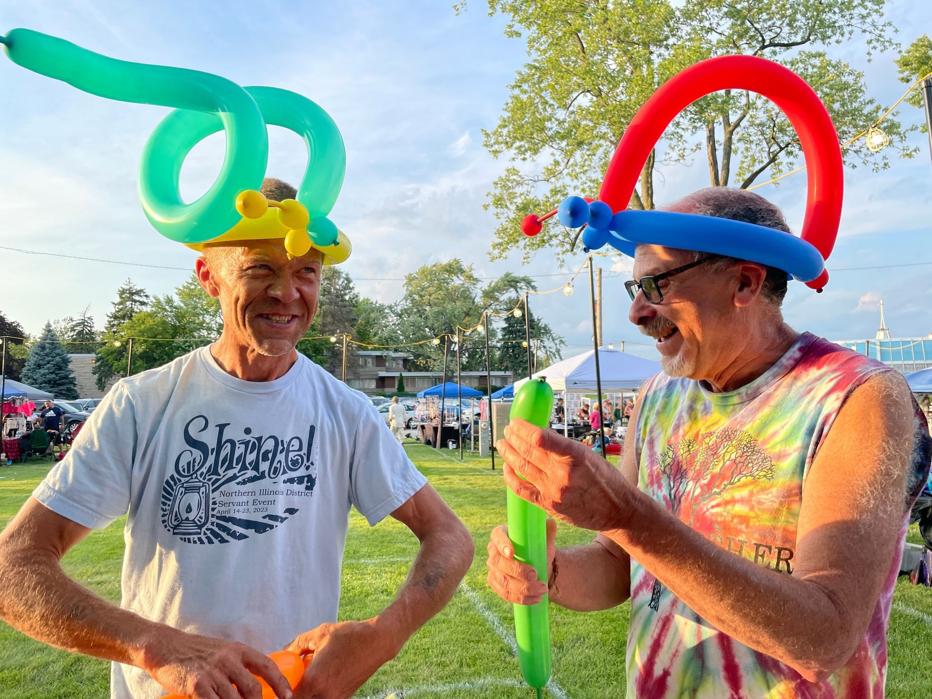 Two men wearing balloon hats are standing next to each other in a field.