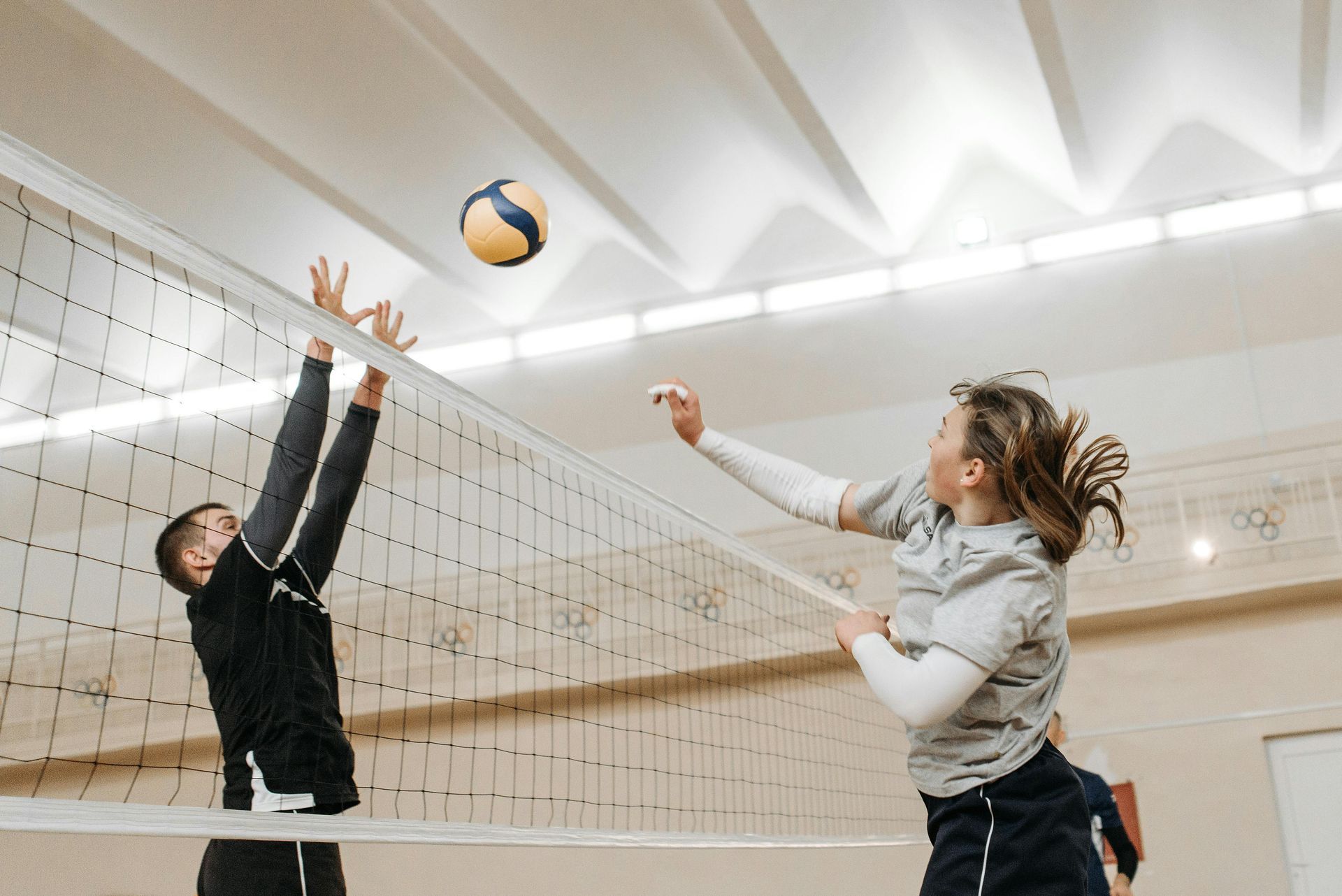 A man and a woman are playing volleyball in a gym.