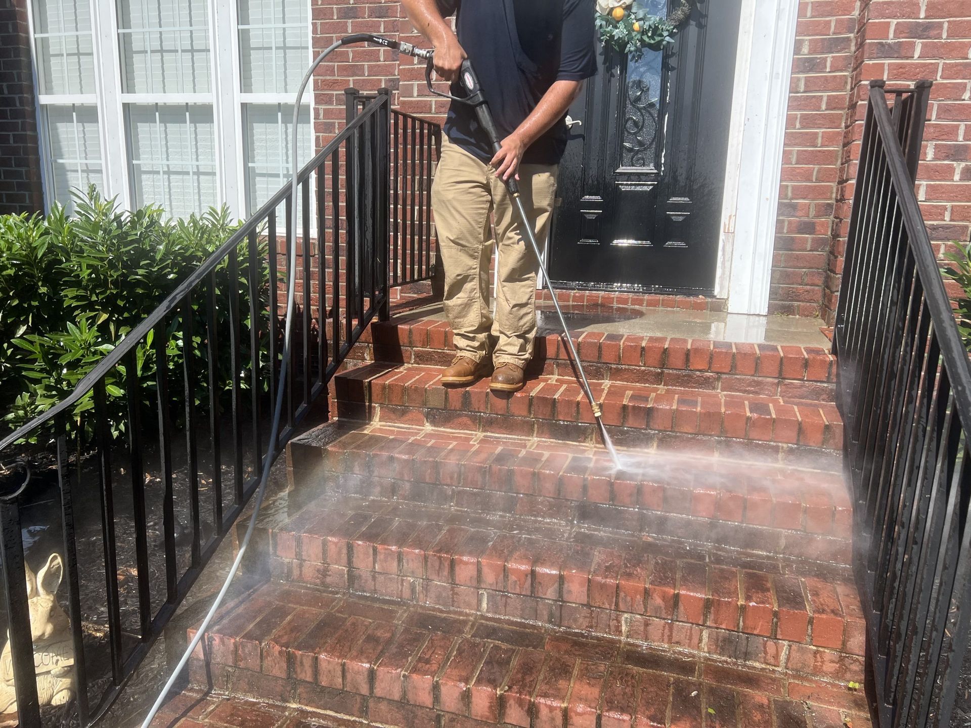 Person power washing brick steps of a house with black railings.
