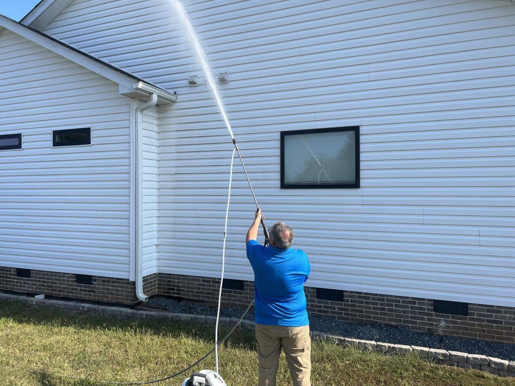 Person power washing the side of a white house with a long nozzle.