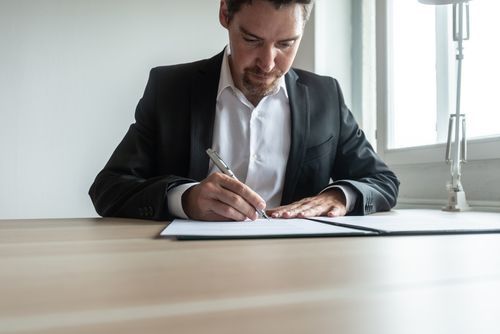 A man in a suit is sitting at a table signing a document.