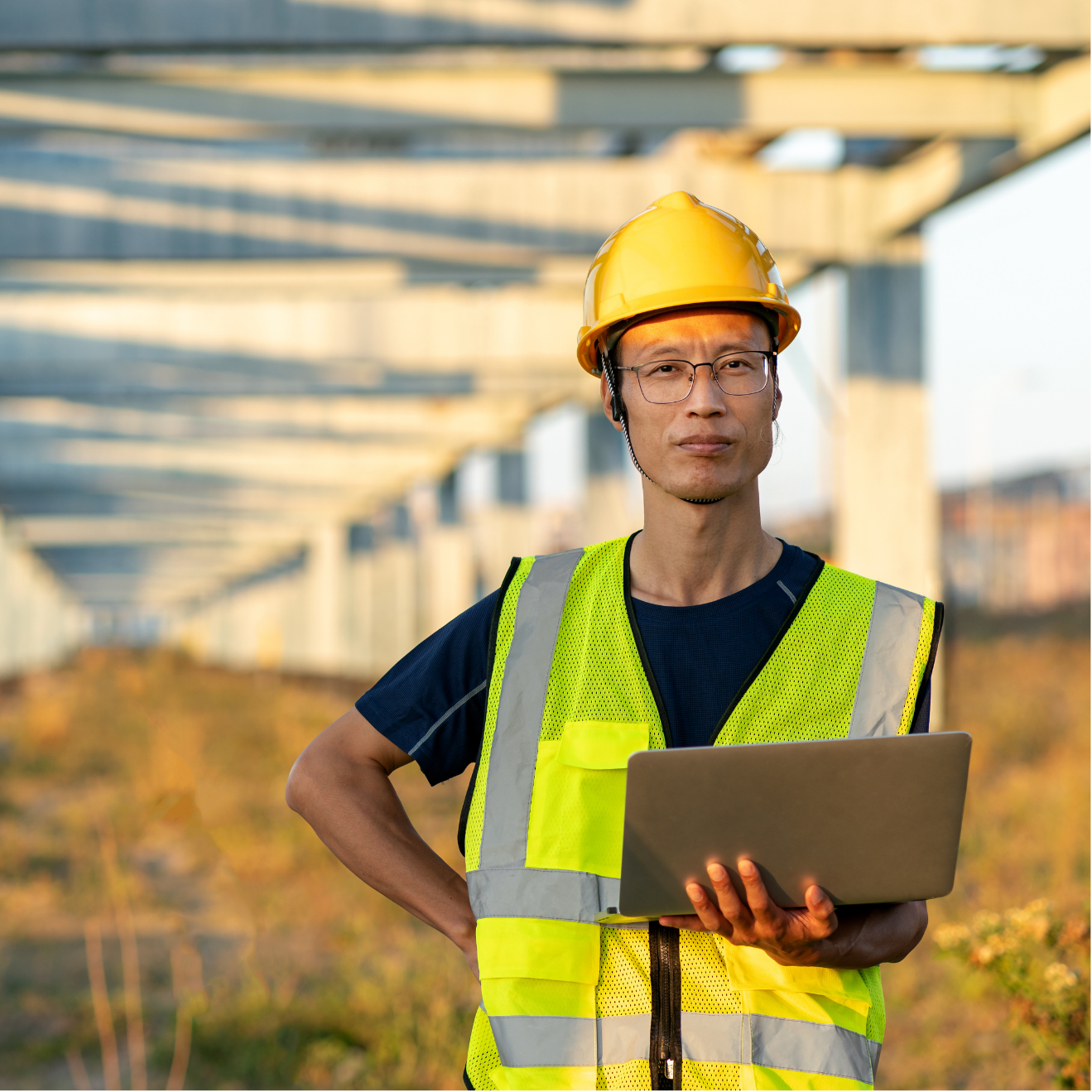 A man wearing a hard hat and safety vest is holding a laptop.