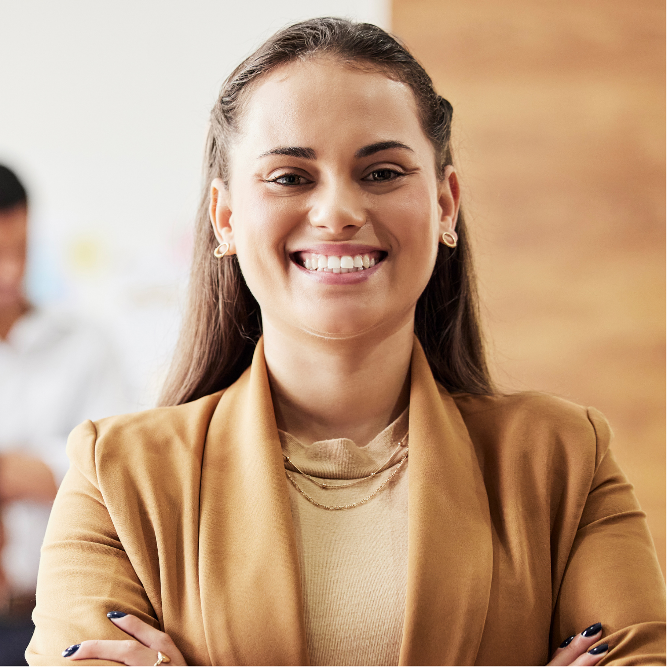 A woman in a brown jacket is smiling with her arms crossed.