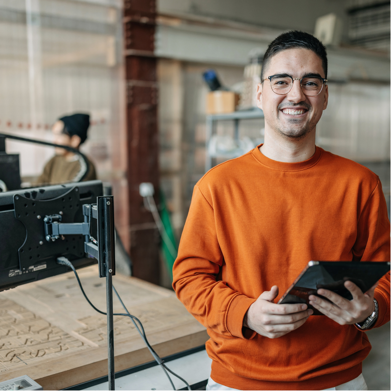A man in an orange sweater is holding a tablet and smiling