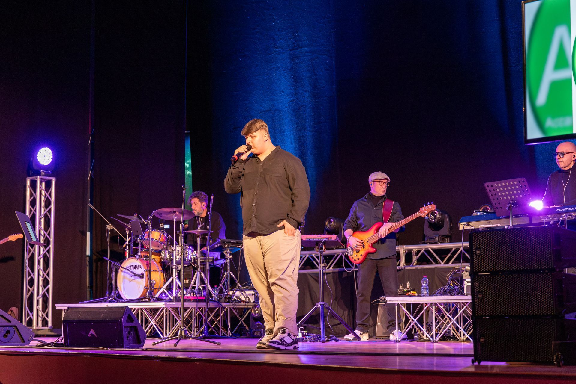 Un uomo canta in un microfono su un palco di fronte a una band.
