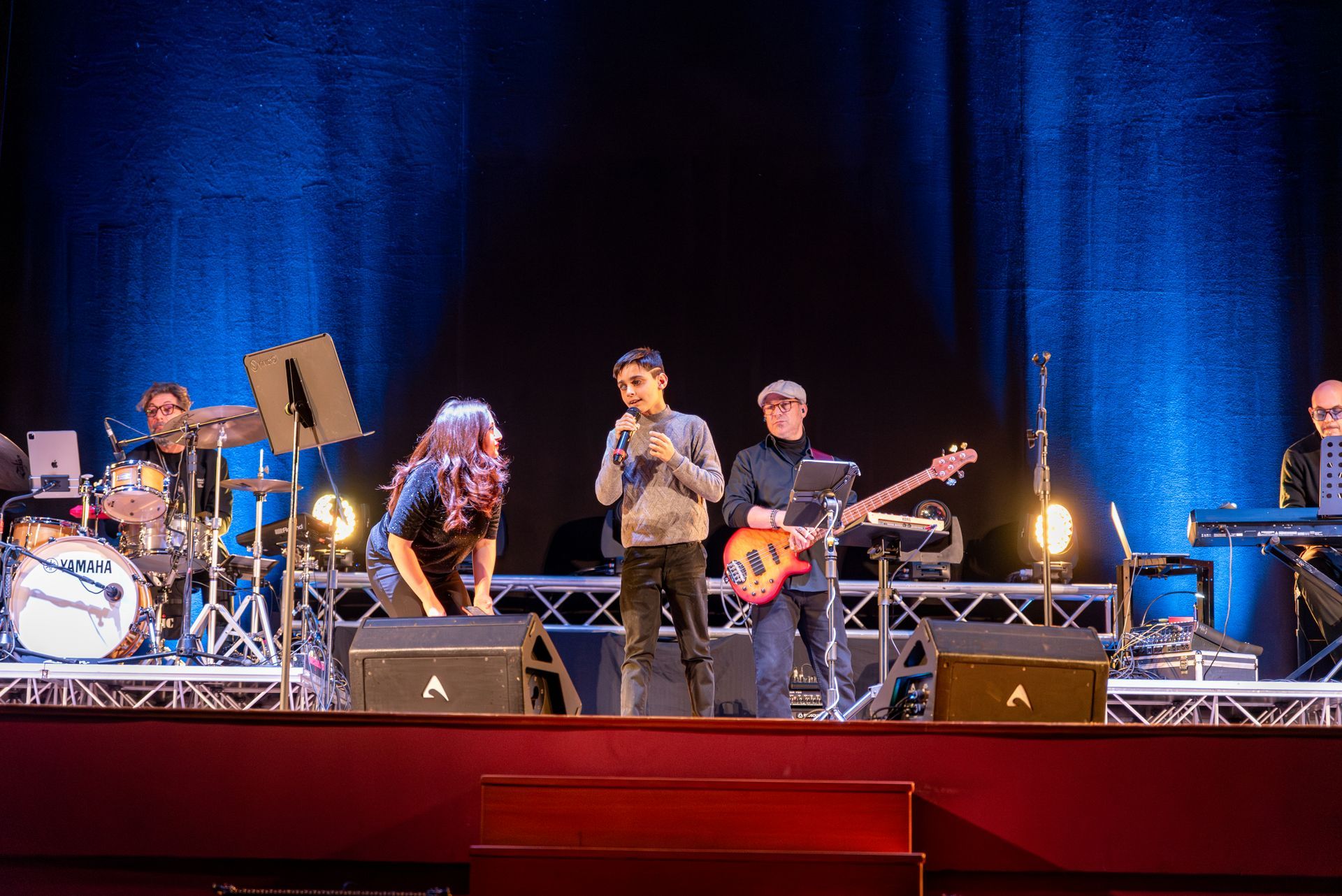 Un gruppo di persone è in piedi su un palco e suona degli strumenti.