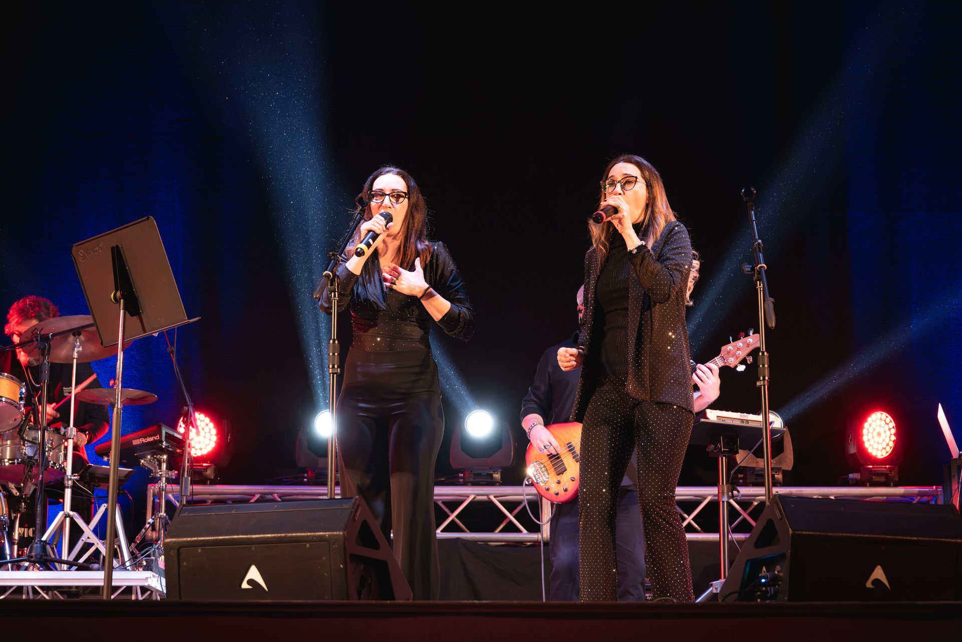 Due donne cantano nei microfoni su un palco.