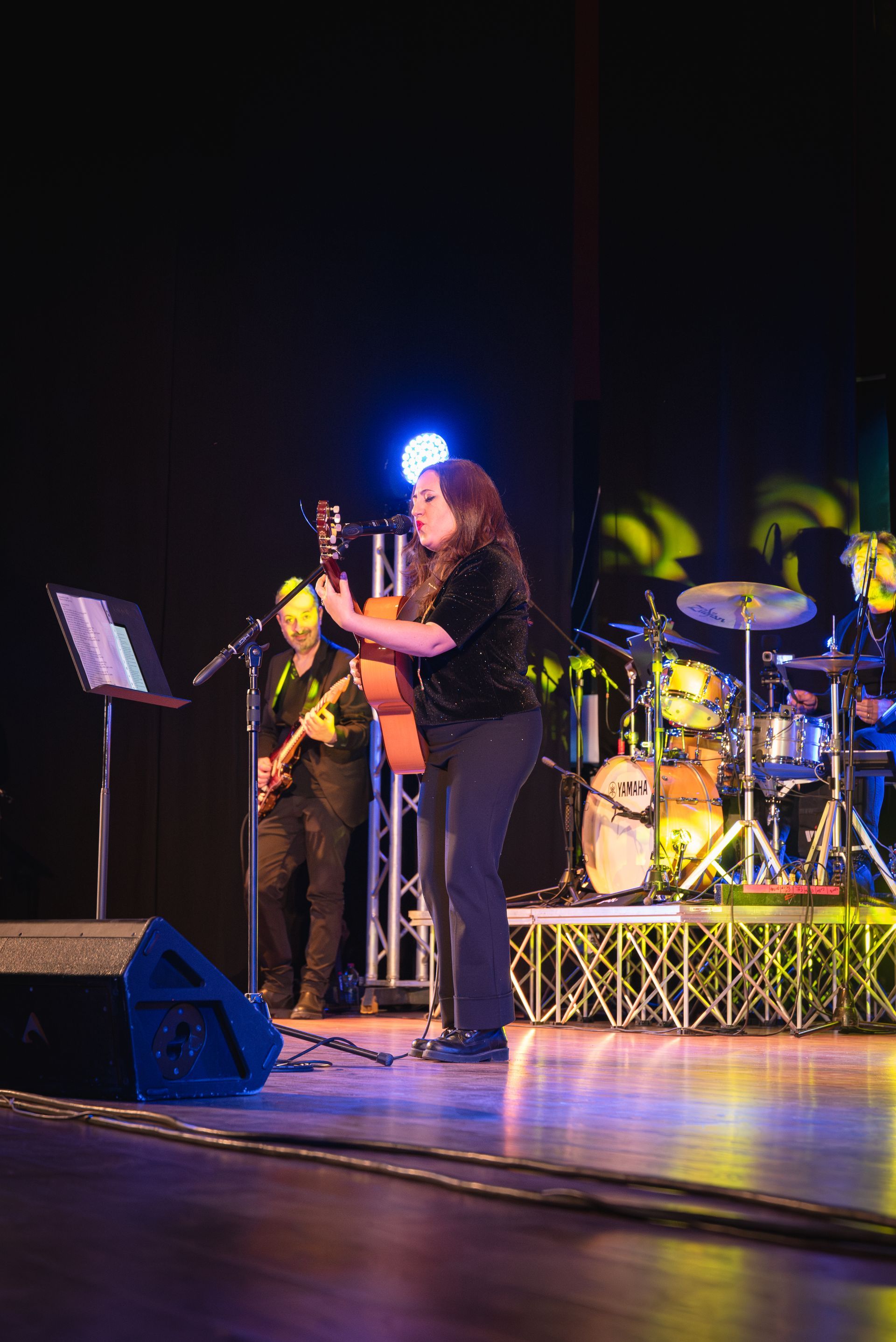 Una donna è in piedi su un palco, suona la chitarra e canta in un microfono.