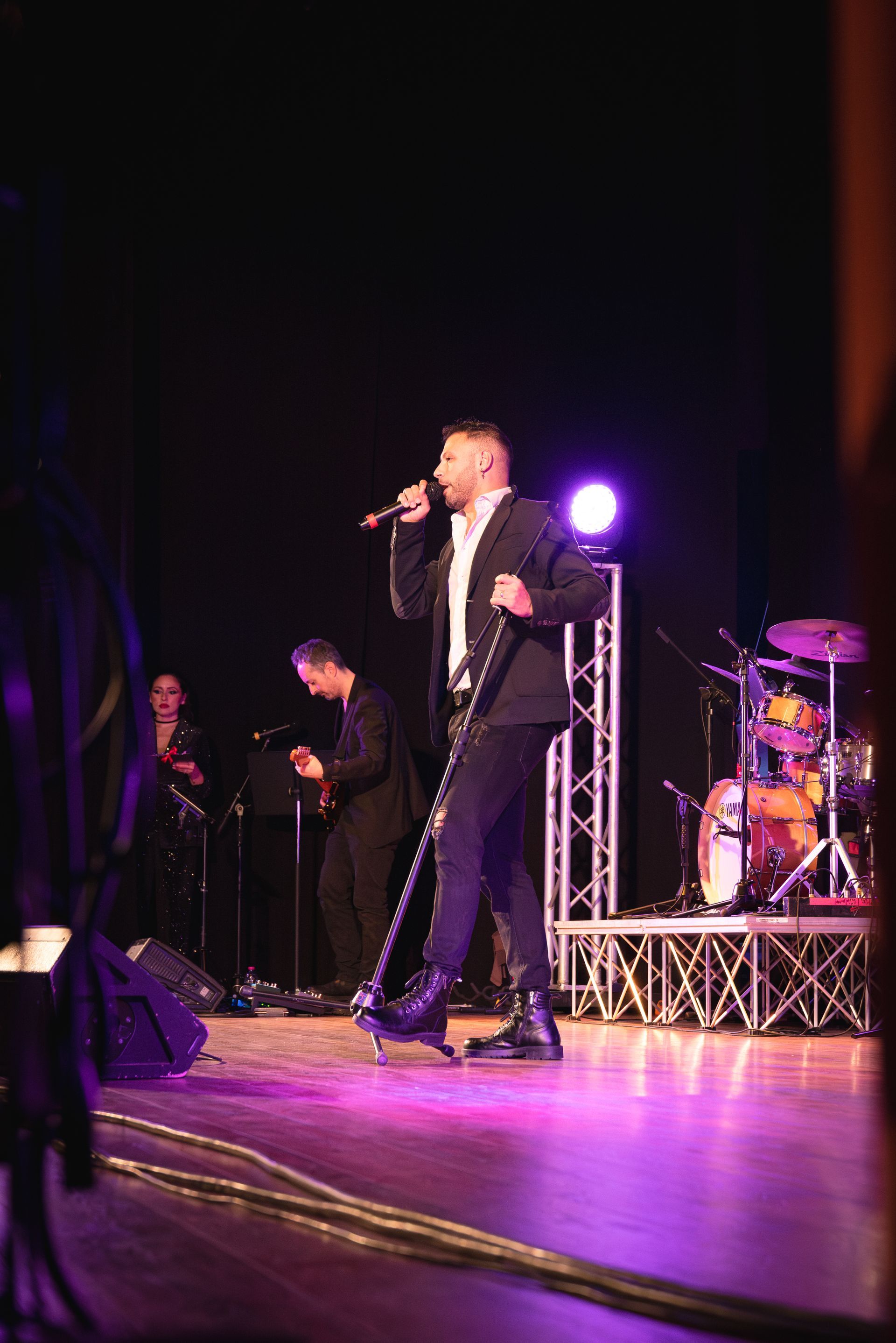 Un uomo in giacca e cravatta canta in un microfono su un palco.