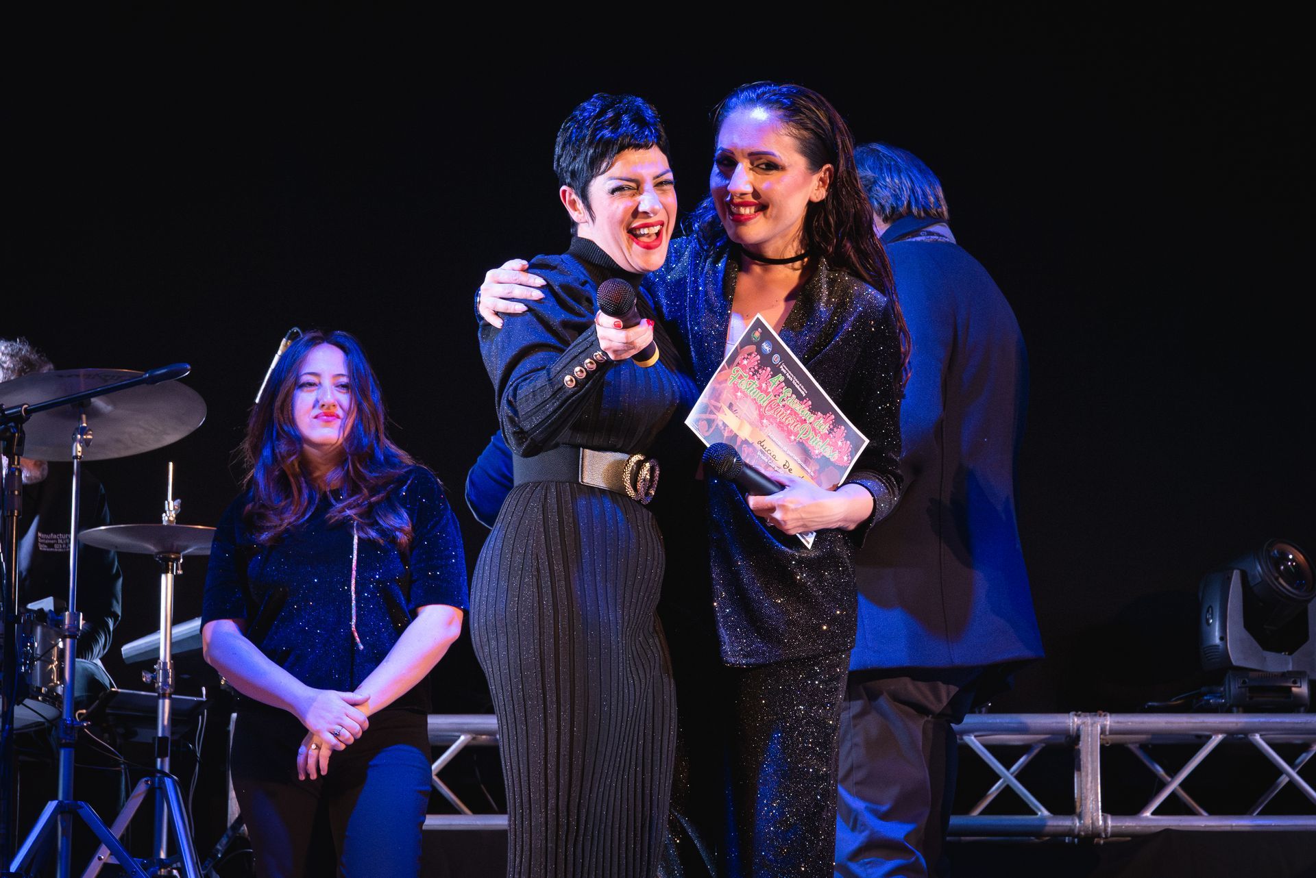 Due donne sono in piedi una accanto all'altra su un palco e tengono in mano un microfono.