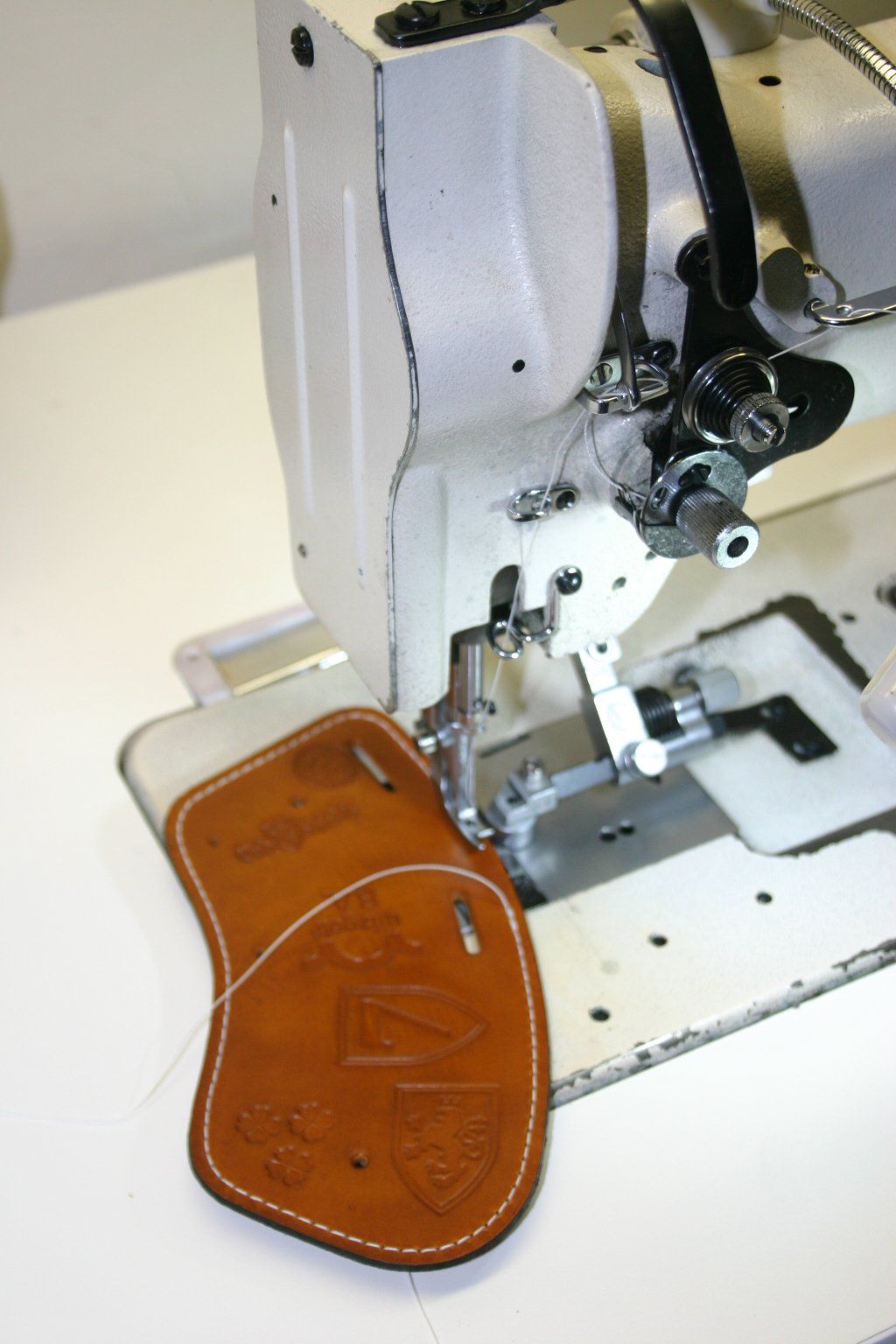 Leather ClubShields being sewn on an industrial sewing machine. Tan leather with white stitching.