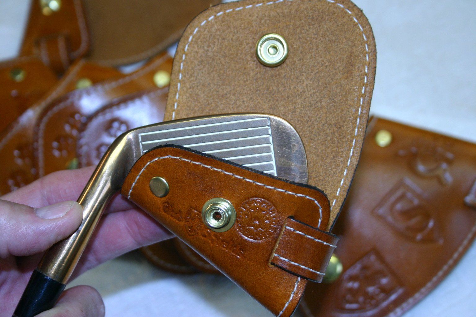 Golf club being put into brown leather headcover. Close up.