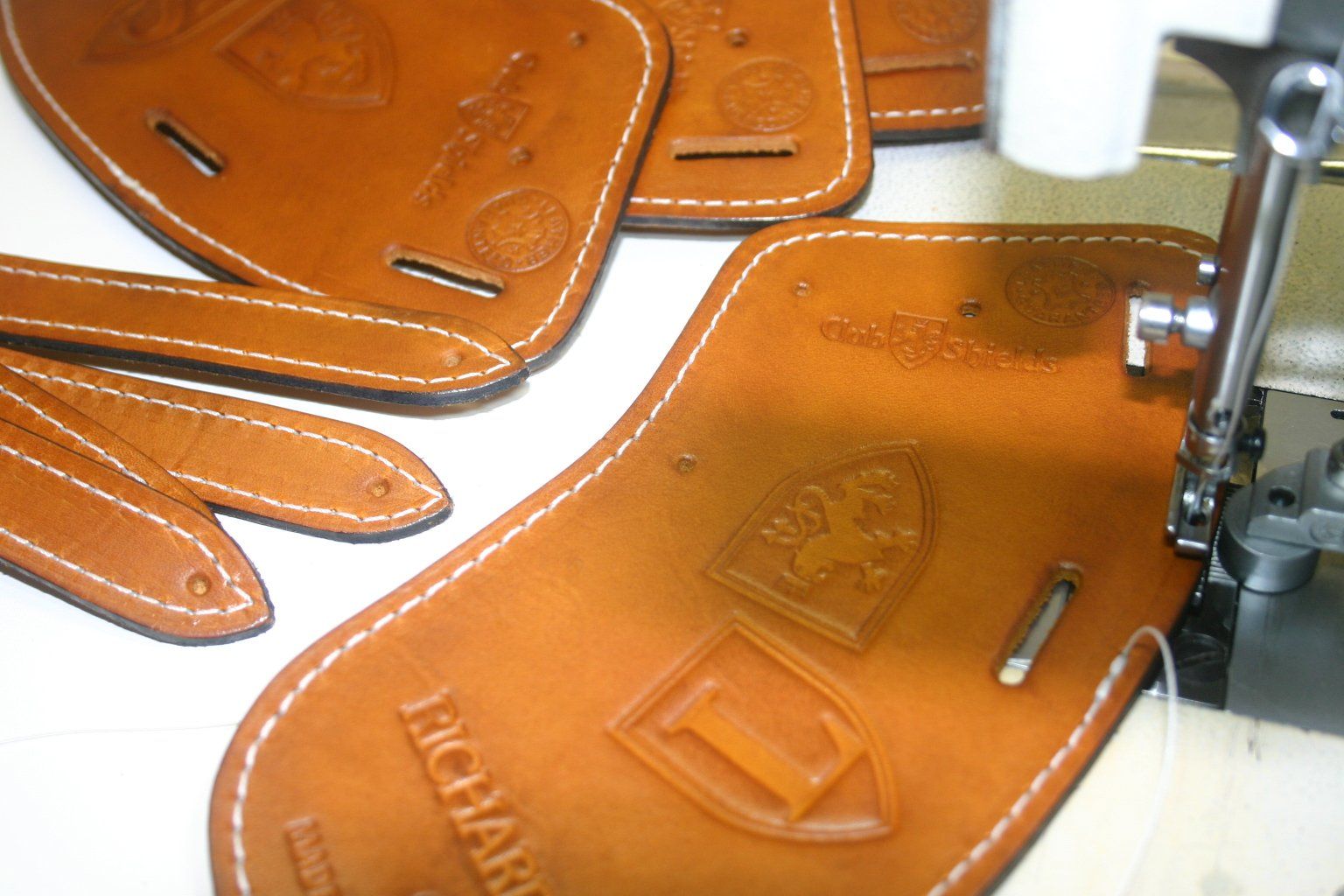 Leather iron covers with logos being sewn with white thread on a sewing machine. Brown leather and white thread.