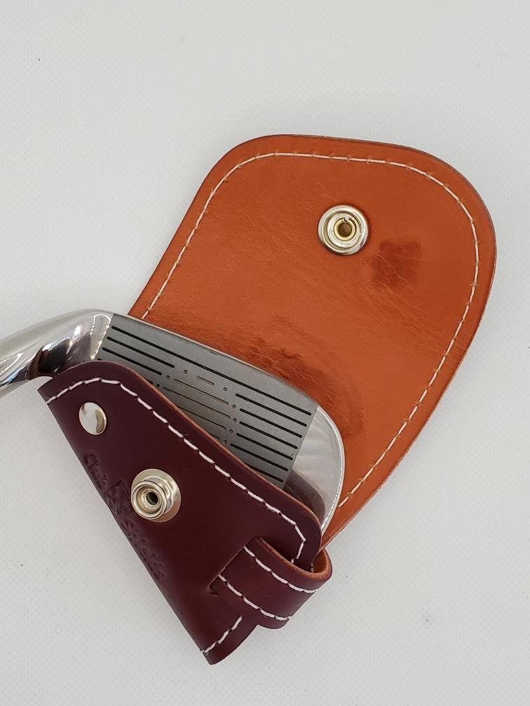 Golf club in a leather head cover, brown and burgundy. White stitching, snap closure.