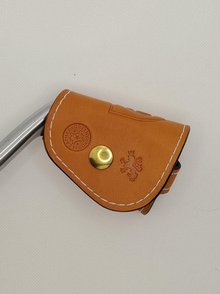 Tan leather pouch with white stitching, brass button, and decorative stamps.