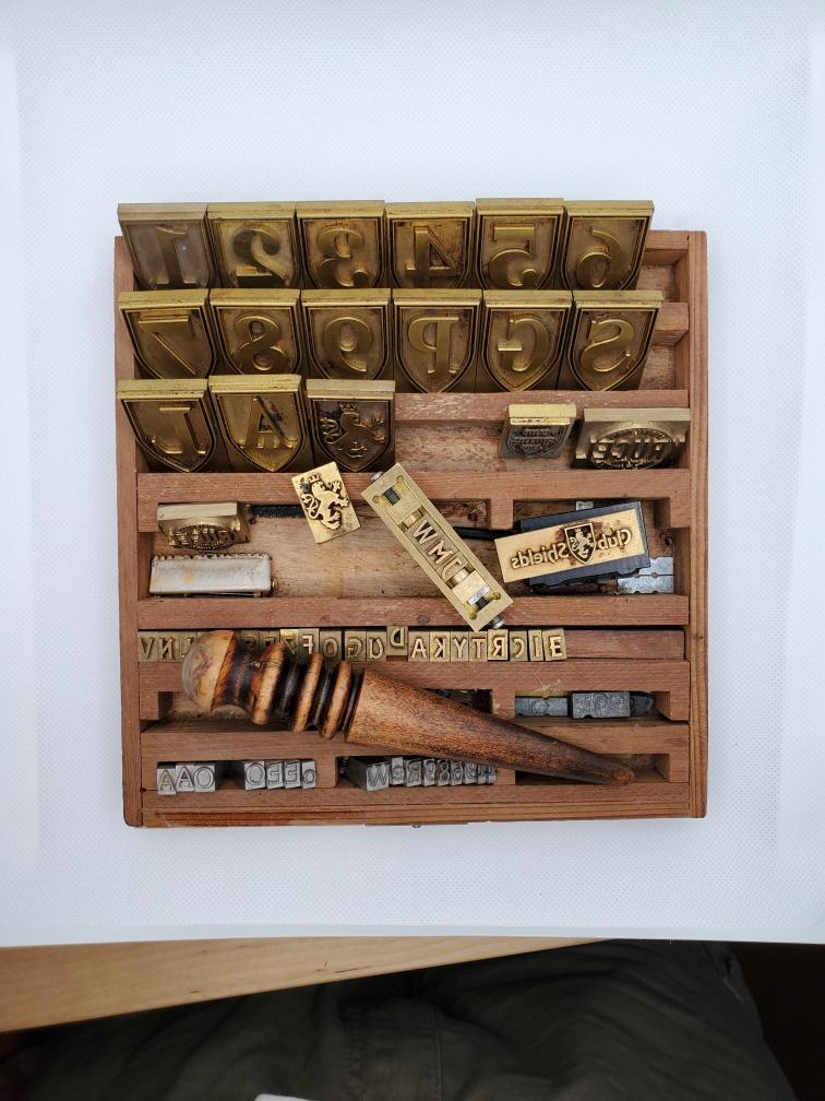 Wooden printing press type tray with brass letters and printing tools.