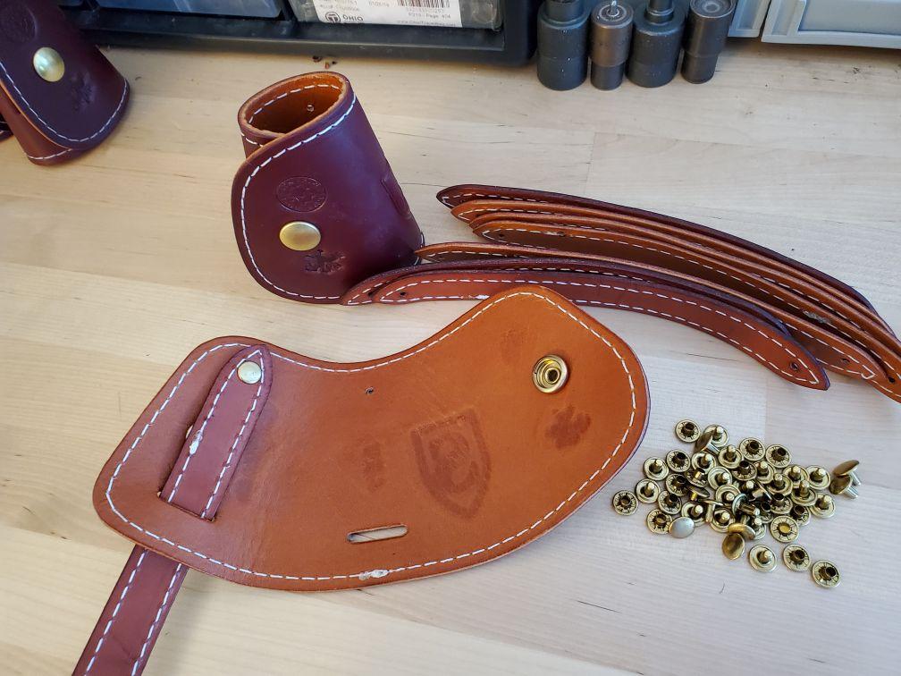 Leather pieces and hardware for crafting, including straps, snaps, and studs, on a wooden surface.