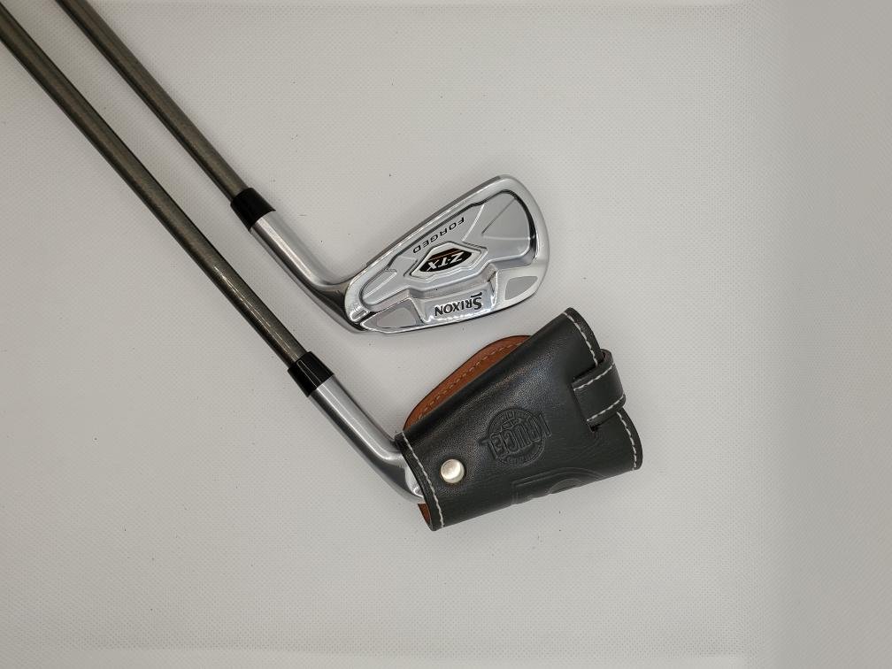 Golf clubs with a black leather club cover on a white surface.