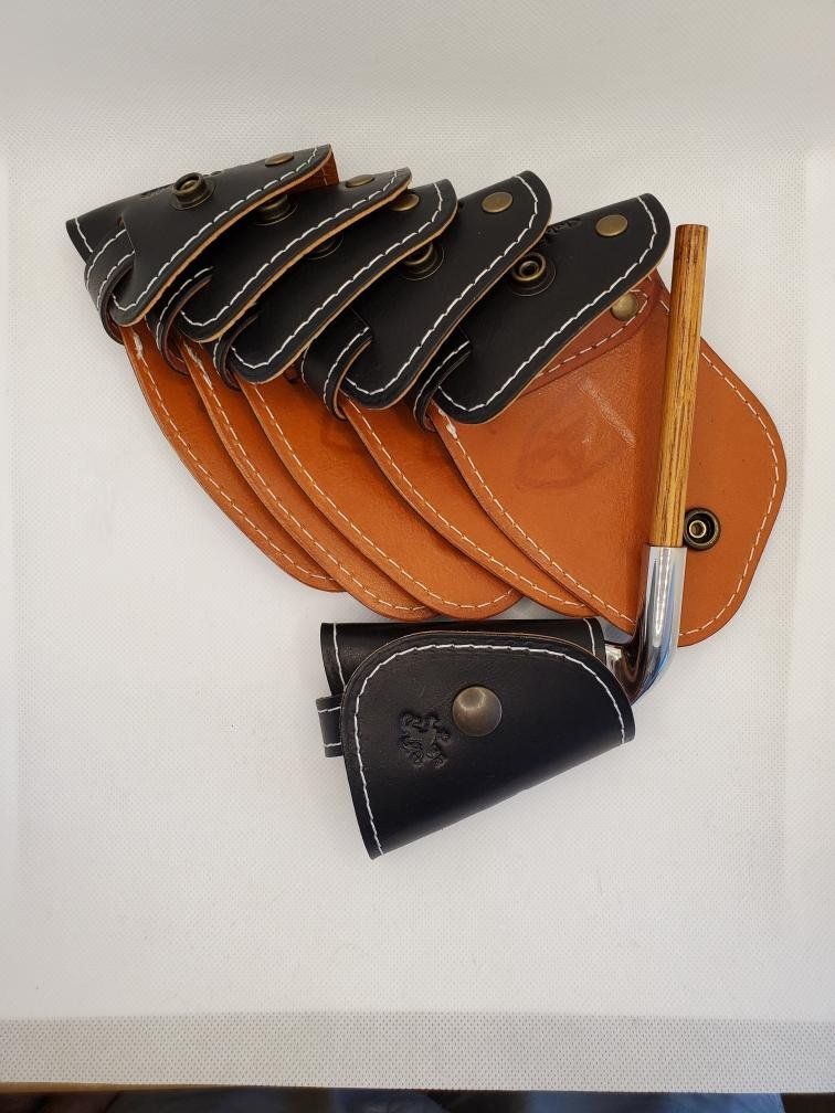 Golf club covers and a golf club, in black and tan leather, arranged on a white surface.