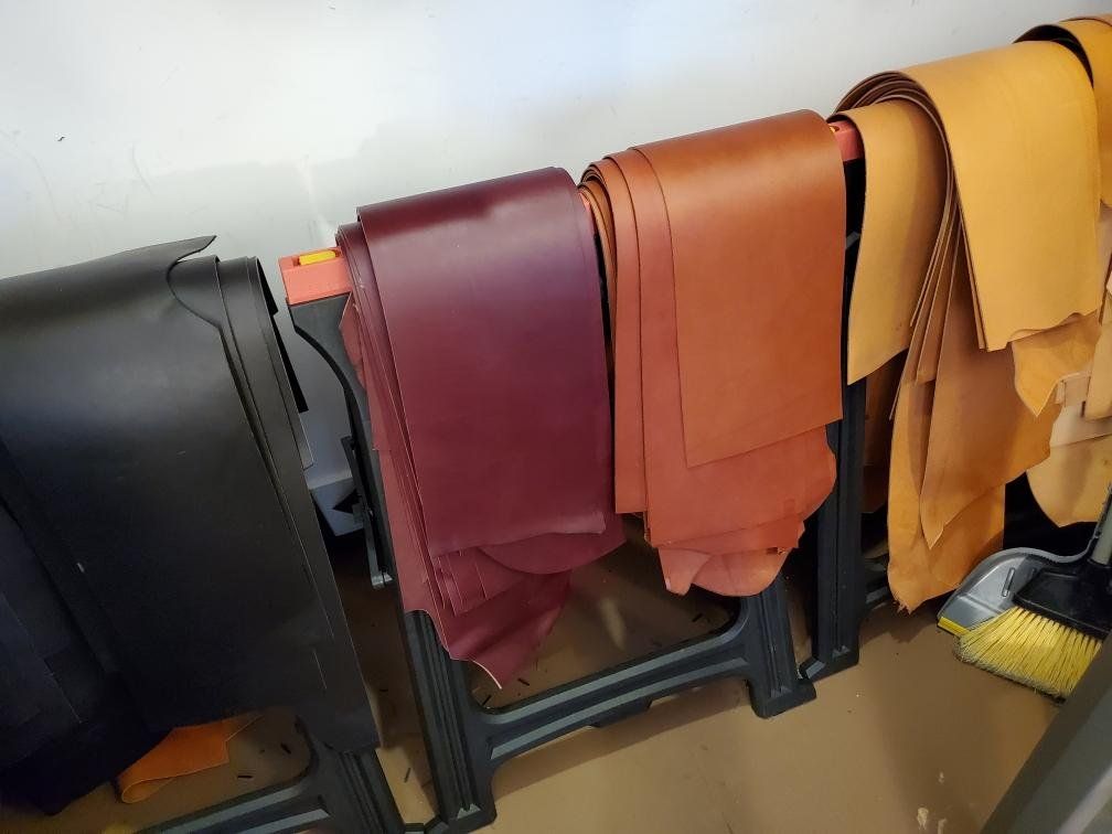 Leather hides in various colors stacked on saw horses.