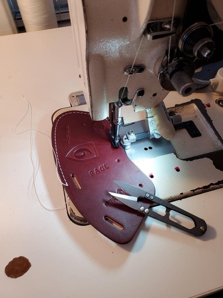 A mahogany leather ClubShield being sewn by a machine, with scissors resting on it. 