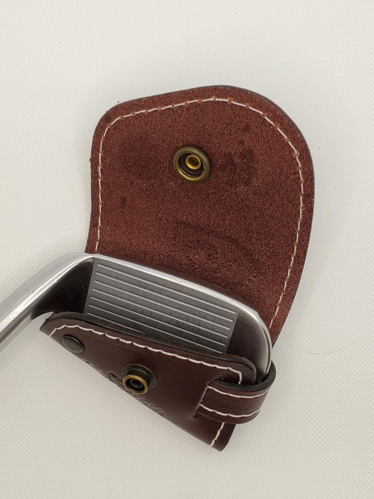 Golf club iron partially inside a brown leather headcover with white stitching.