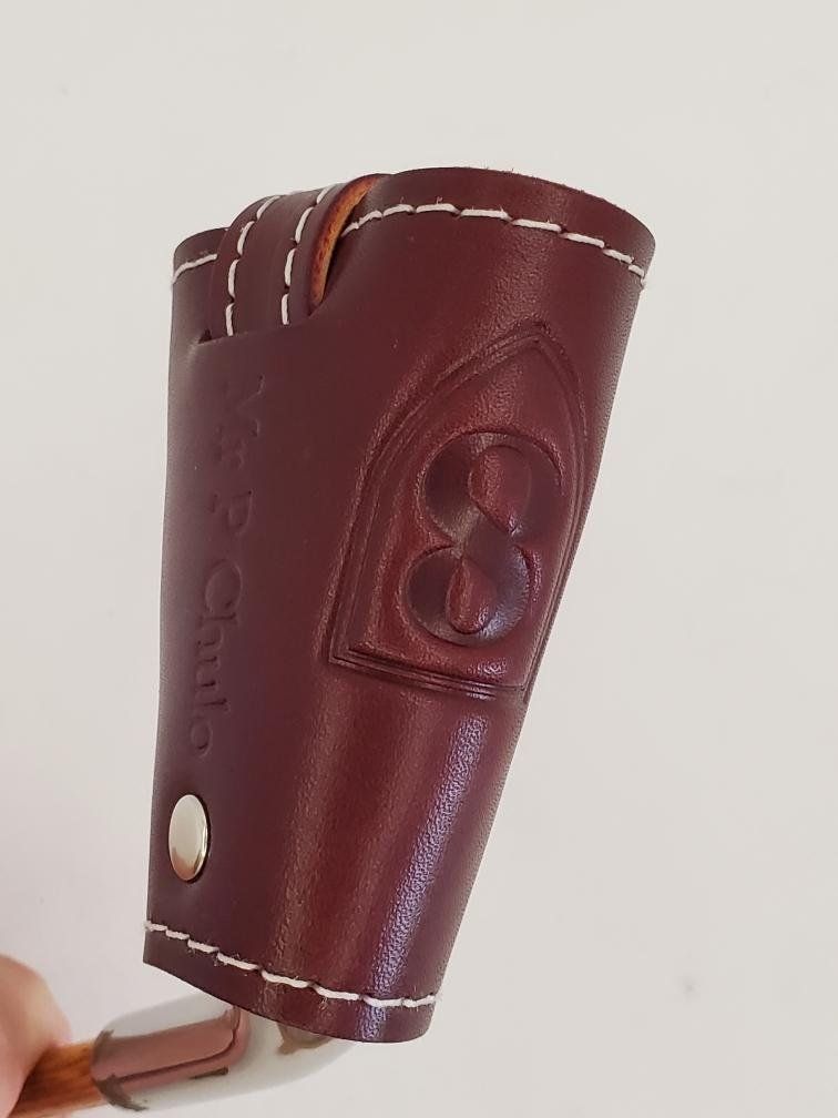 Mahogany leather holster with white stitching and ornate design; holds a wooden handle.