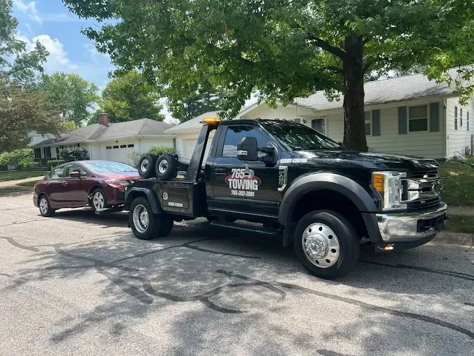Black tow truck towing a maroon car on a residential street.