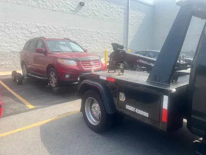 Red SUV being towed onto a flatbed tow truck in a parking lot.