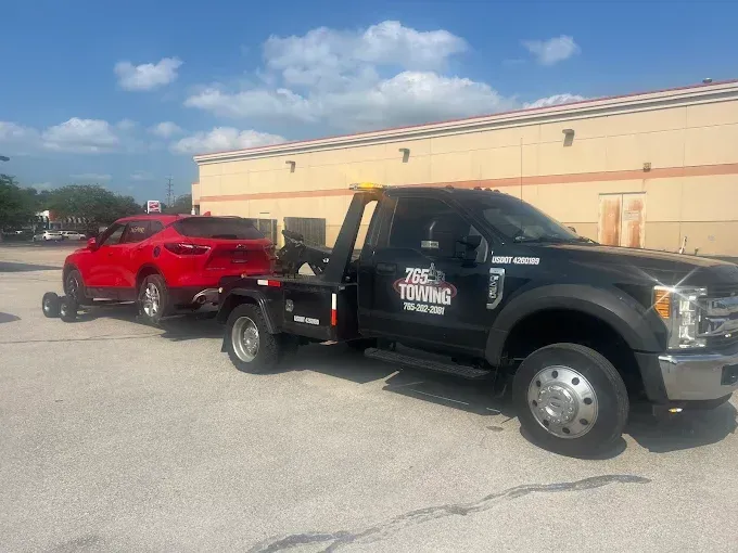 Black tow truck towing a red car in a parking lot on a sunny day.
