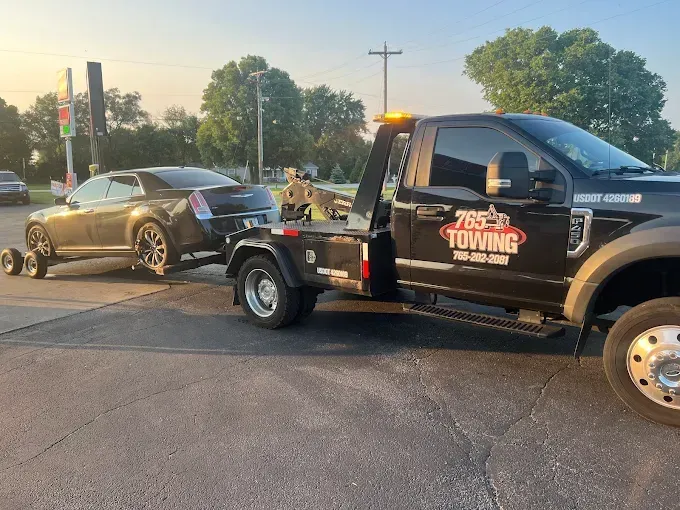 A black Chrysler 300 being towed by a black tow truck. The tow truck has an orange flashing light.