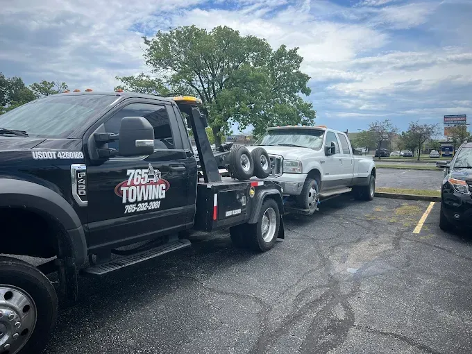Tow truck towing a white pickup truck in a parking lot on a cloudy day.