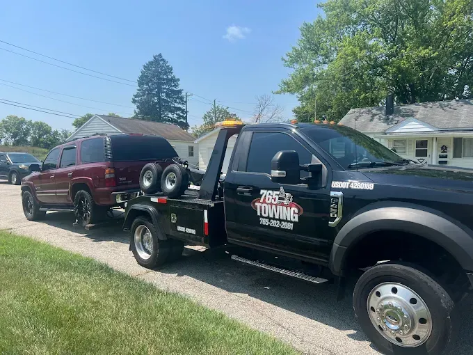 Tow truck towing a maroon SUV on a sunny residential street. 