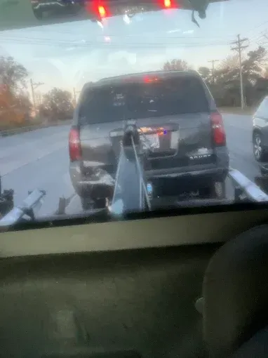 Dark SUV being towed on a flatbed tow truck on a road.