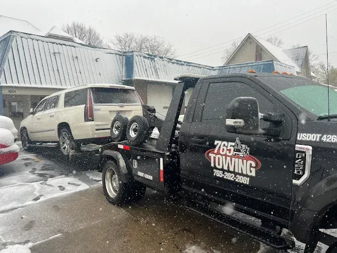 A white SUV being towed by a black tow truck in a snowy environment.