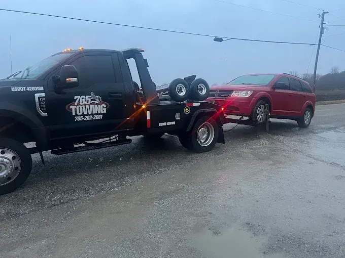 Black tow truck towing a red SUV on a gray, overcast day.