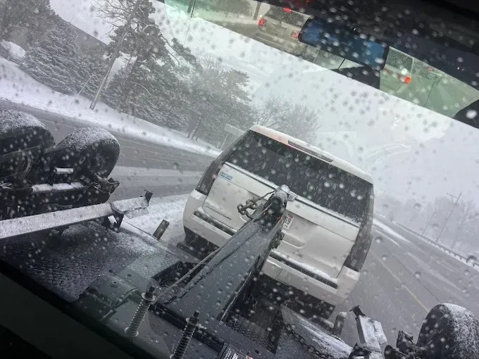 White SUV being towed on a snowy road, viewed from a tow truck, with falling snow.