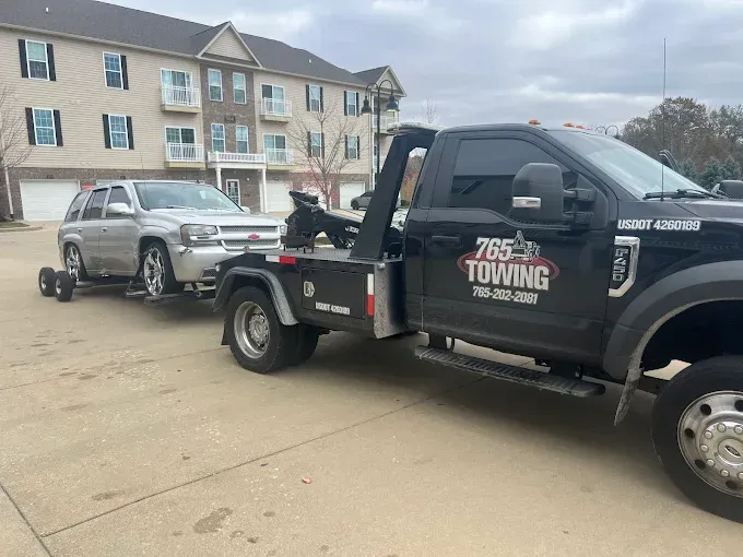 Tow truck towing a silver SUV in front of an apartment building.