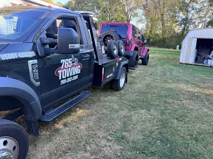 Tow truck loading a pink Jeep on a grassy yard.