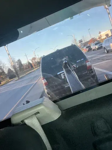 View from inside a vehicle, looking at a black minivan being towed on a sunny day.