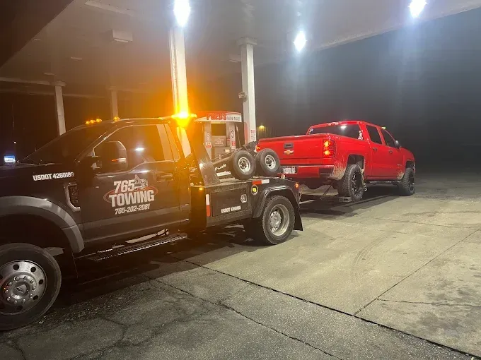 Tow truck towing a red pickup truck at a gas station at night.