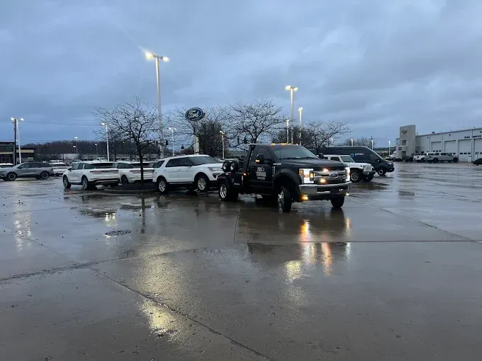 Dark truck in a wet parking lot, other vehicles in background under overcast sky.