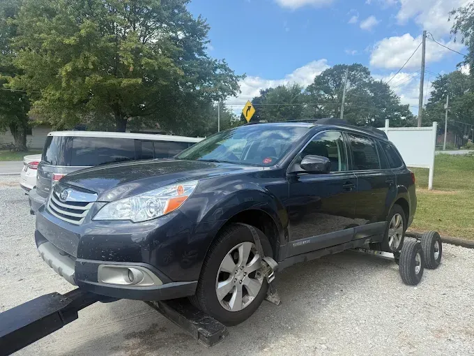 Dark blue Subaru Outback on a tow truck, parked on gravel.