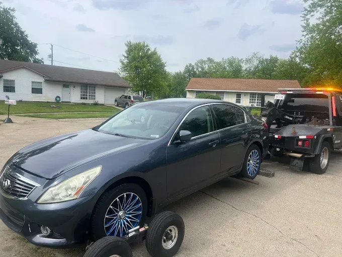 A dark gray sedan being towed by a tow truck on a residential street. Blue rims.